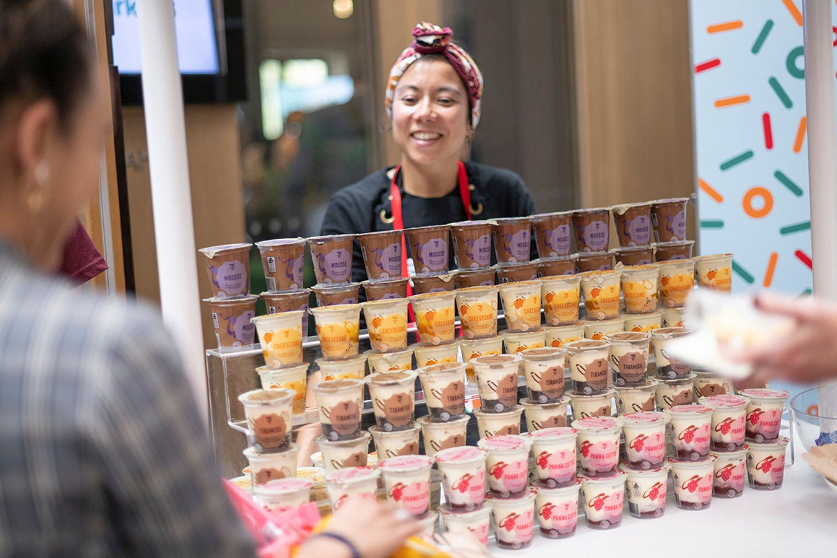 A picture of a 7-Eleven team member smiling - she is standing behind a display of new products