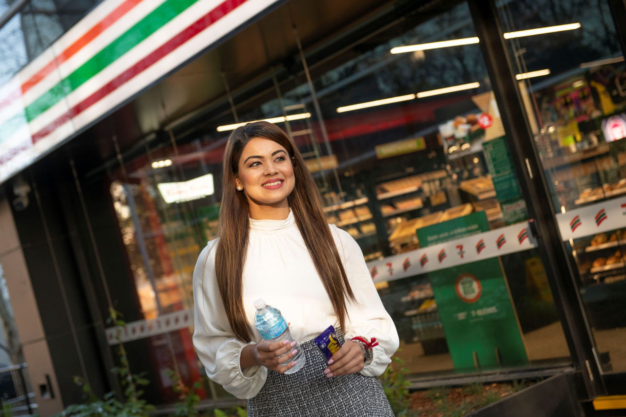 Customer walking out of a 7-Eleven store holding a water and apple in their hands.